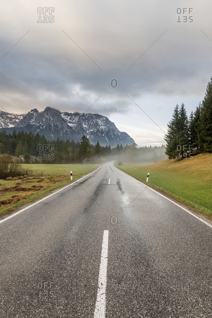 Early morning on the country road at schmalensee near mittenwald, the road is wet with rain, light fog rises and the karwendel towers in the background