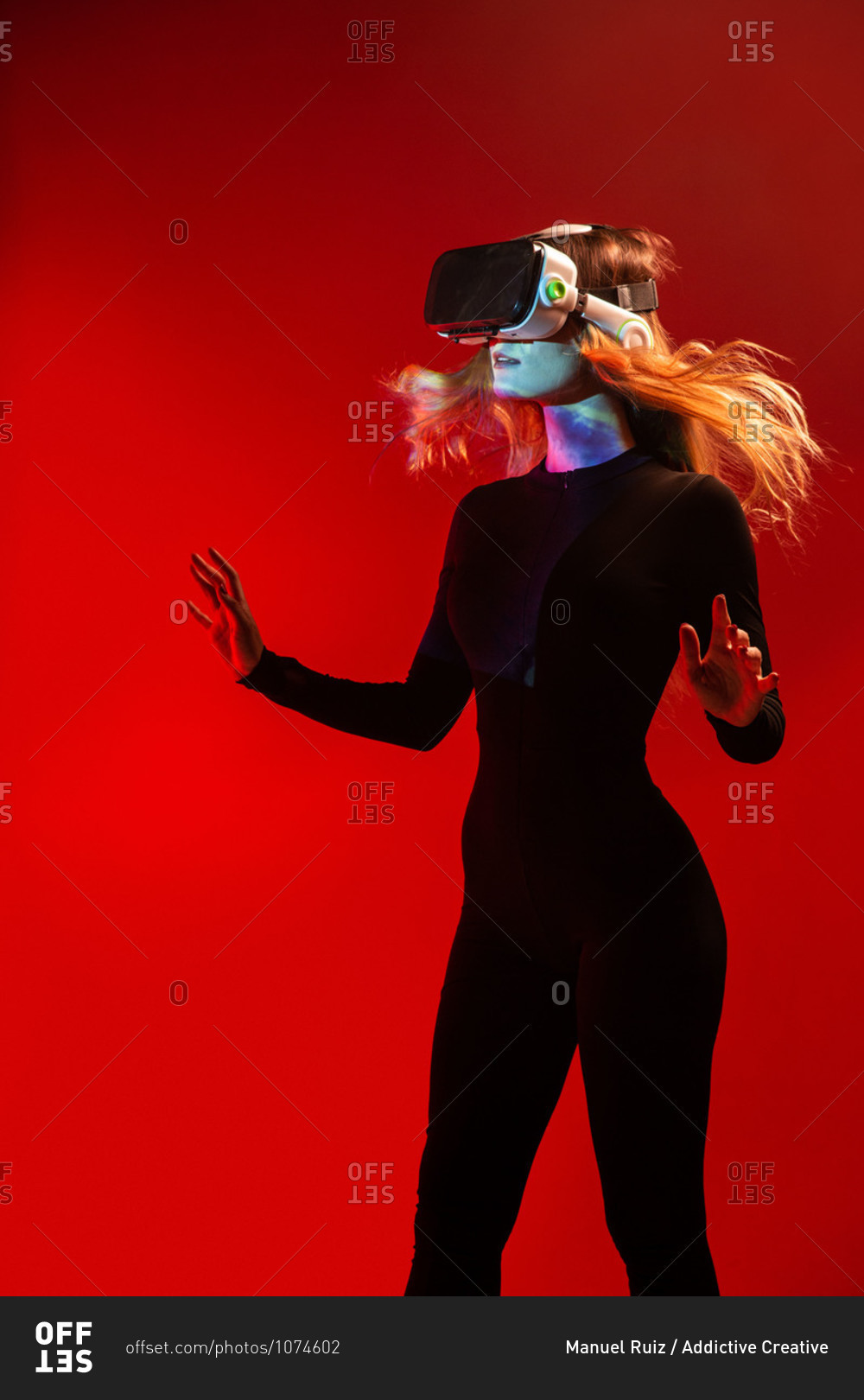 Side view of young unrecognizable blonde woman standing touching air and wearing virtual reality headset on colorful red studio background