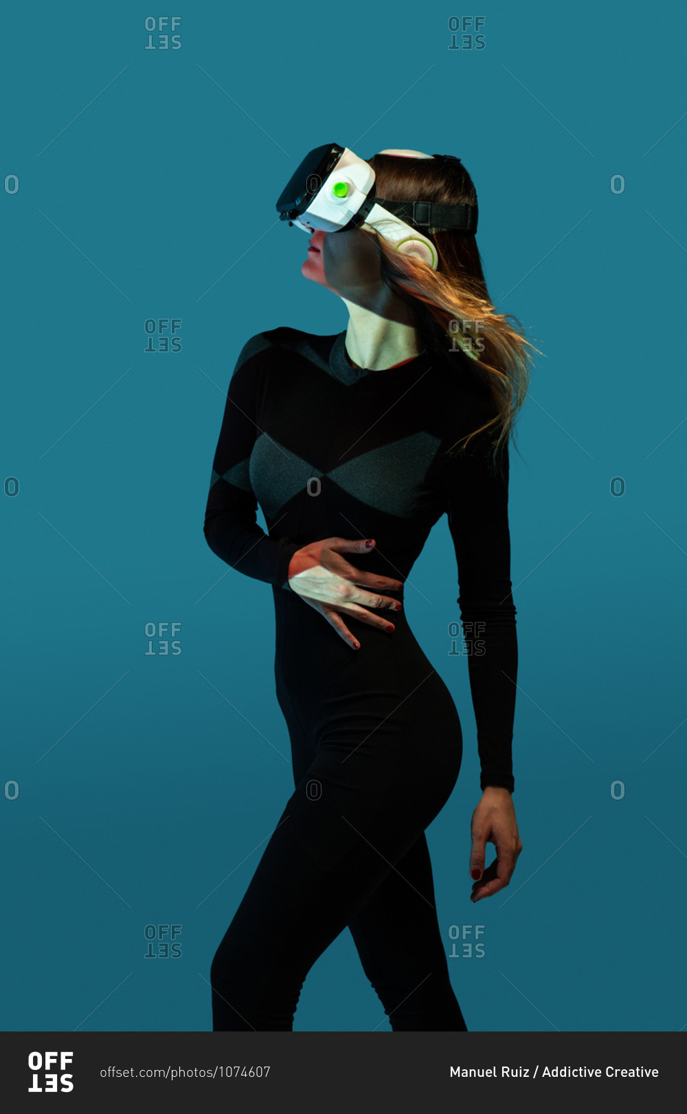 Side view of young unrecognizable blonde woman standing wearing virtual reality headset on colorful blue studio background