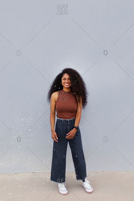 Optimistic African American young female with curly hair standing in city with flying confetti while looking at camera