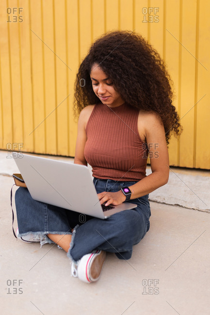 Cheerful African American self employed woman sitting on street with laptop