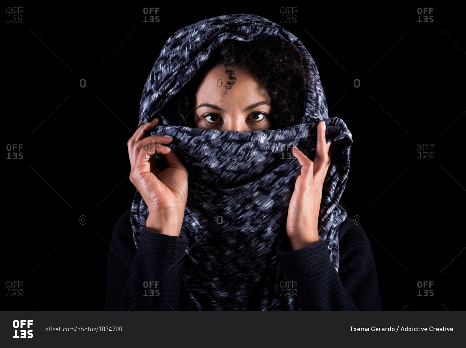 Serious young black female hiding half face with headscarf and looking at camera against dark background