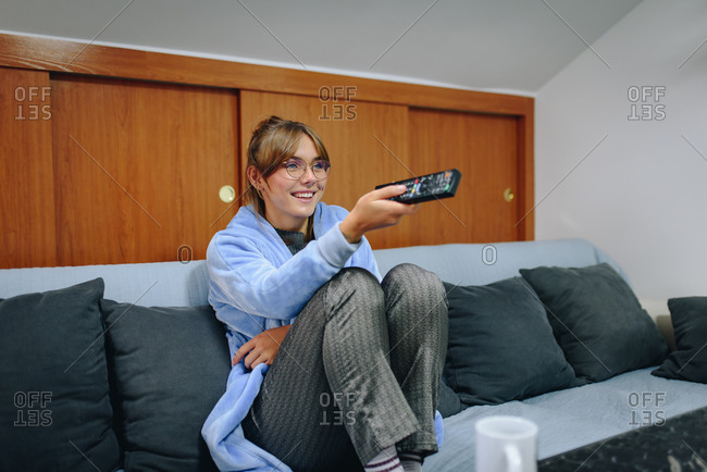 Girl sitting on a sofa in a robe and using a remote control television