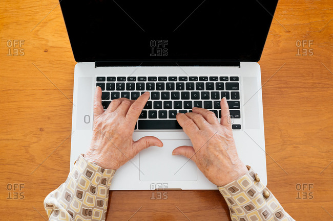 Senior female typing on modern netbook while sitting at table at home and reading news on social media