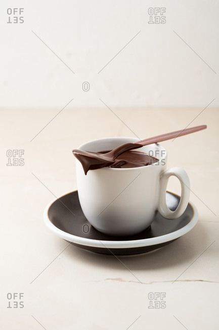 Chocolate pudding in white cup on light table with spoon on top of mug