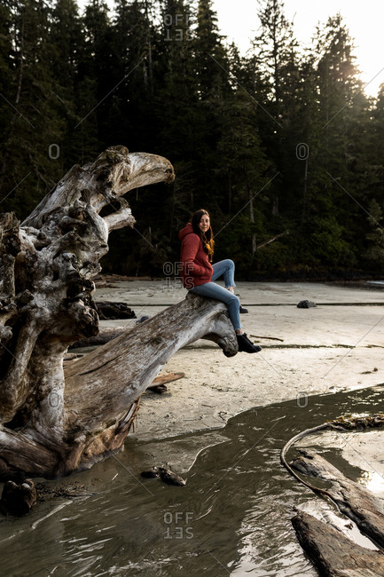 Female exploring the beach with forest and trees on a piece of driftwood