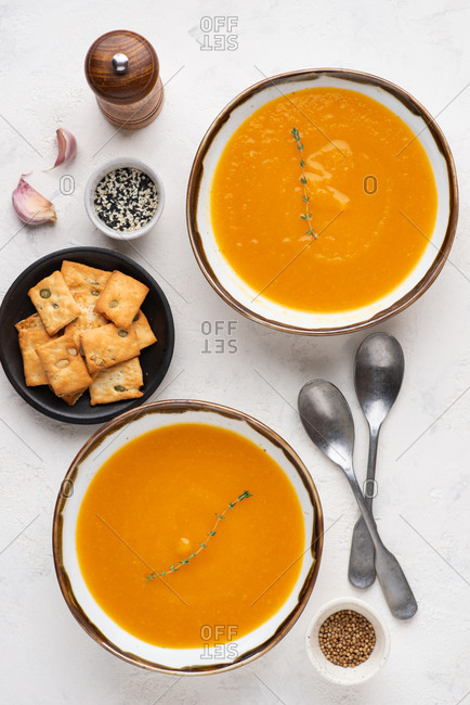 Overhead view of two bowls of pumpkin soup served with cheese biscuits with pumpkin seeds