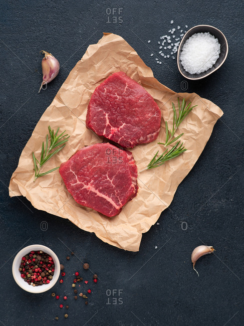 Raw beef steak over dark background with rosemary, sea salt, garlic and spices