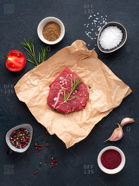 Raw beef steak over dark background with rosemary, sea salt, garlic and spices