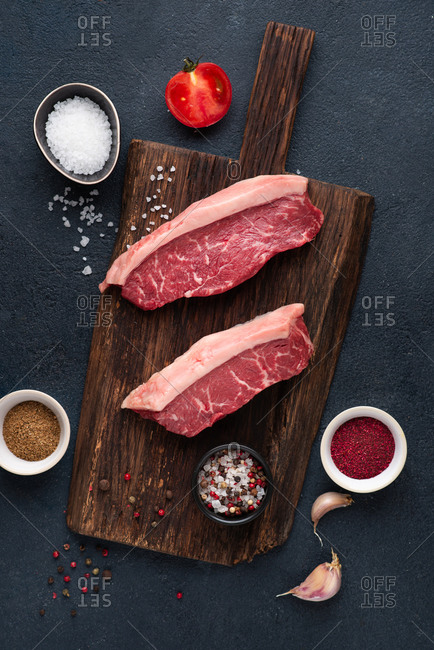 Raw beef black angus steaks over dark background with garlic and spices