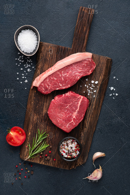 Raw beef steak variety over dark background with rosemary, sea salt, garlic and spices
