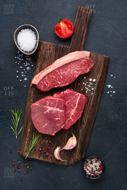 Raw beef steak variety over dark background with rosemary, sea salt, garlic and spices