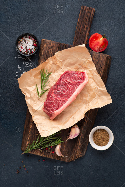 Raw beef black angus steak over dark background with rosemary, sea salt, garlic and spices