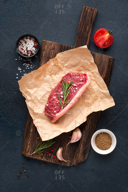 Raw beef black angus steak over dark background with rosemary, sea salt, garlic and spices