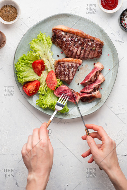 Top view of grilled beef black angus steak served with leaf salad. Person cutting a piece of steak