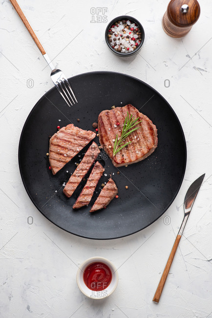Top view of grilled beef steak served on black ceramic plate
