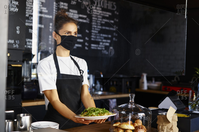Female barista wearing protective mask while serving pasta in coffee shop
