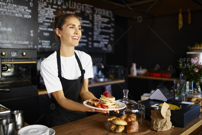 Smiling female barista giving pancakes in plate at cafe