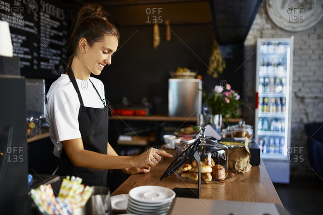 Smiling barista using digital tablet at kitchen counter in cafe