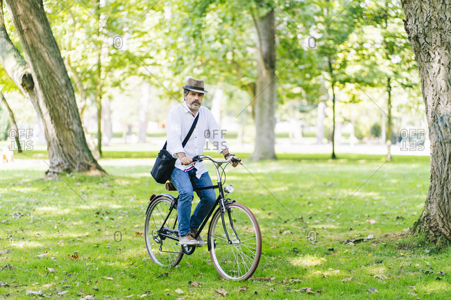 Mature man wearing hat cycling in park