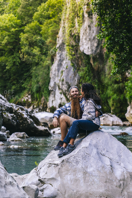 Happy young couple sitting on rock while hiking in Picos De Europa mountain- Asturias- Spain