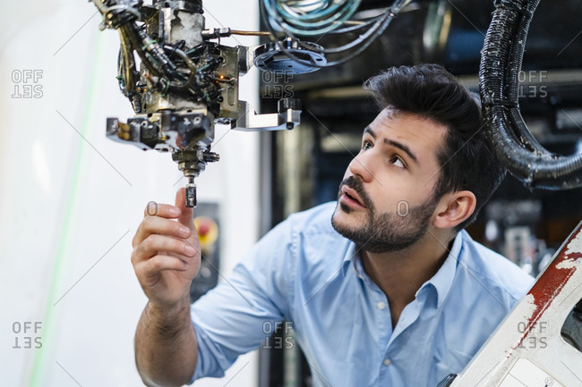Male entrepreneur concentrating while analyzing robotic arm in manufacturing factory