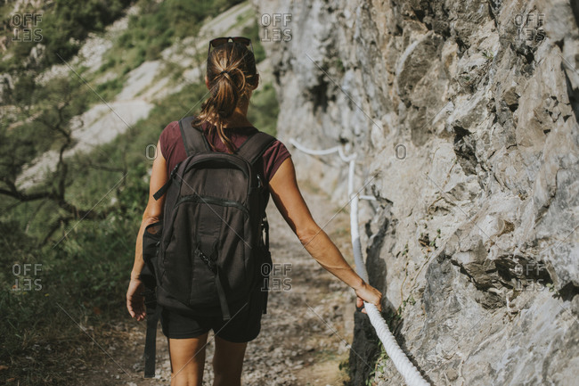 Female trekker with backpack moving downhill while holding rope on rock formation