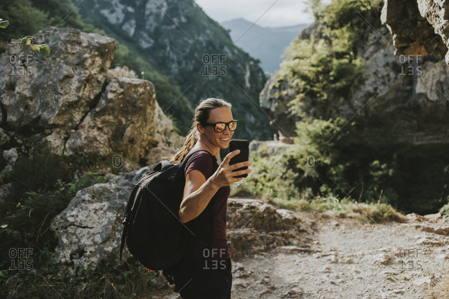 Smiling female trekker taking selfie through smart phone while hiking