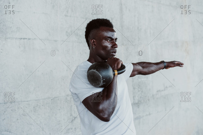 Male athlete with arms outstretched practicing with kettle bell against wall