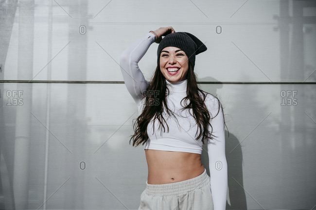 Happy woman wearing knit hat while standing against wall