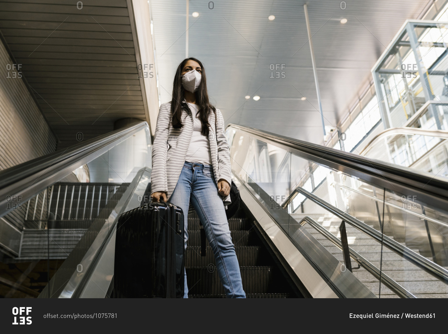 Woman wearing face mask while standing with luggage on escalator at subway station