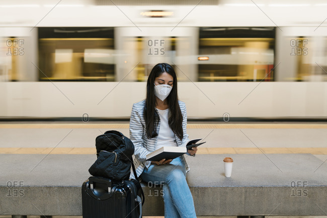 Woman reading book while sitting against moving train at metro station