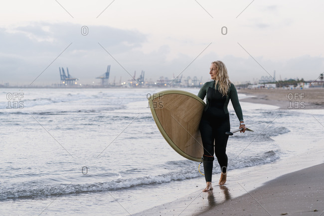 Blond woman holding paddleboard walking at beach during dawn