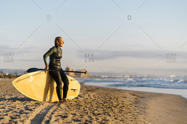 Smiling mature woman with paddleboard looking at sea during dawn