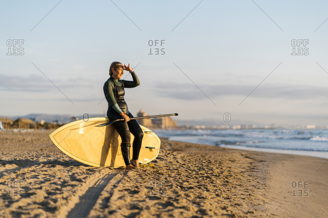 Mature woman with paddleboard looking at sea during dawn