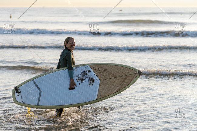 Woman laughing while holding paddleboard standing in sea during dawn