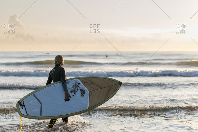 Mature woman holding paddleboard looking at sea while standing in water at dawn
