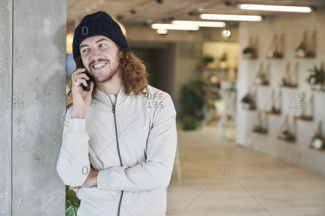 Smiling man wearing knit hat talking on smart phone while standing at home