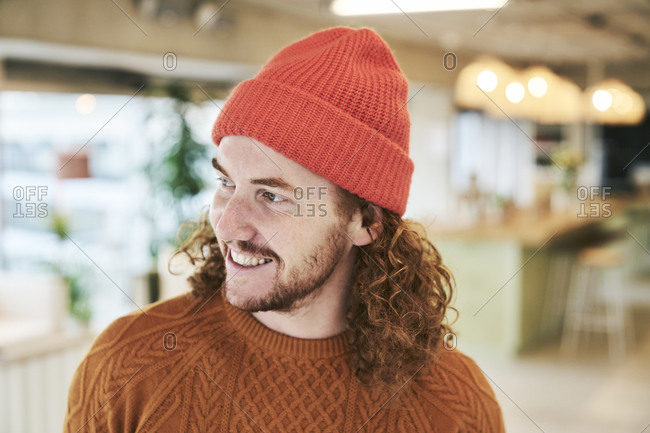 Smiling hipster man wearing red knit hat at home