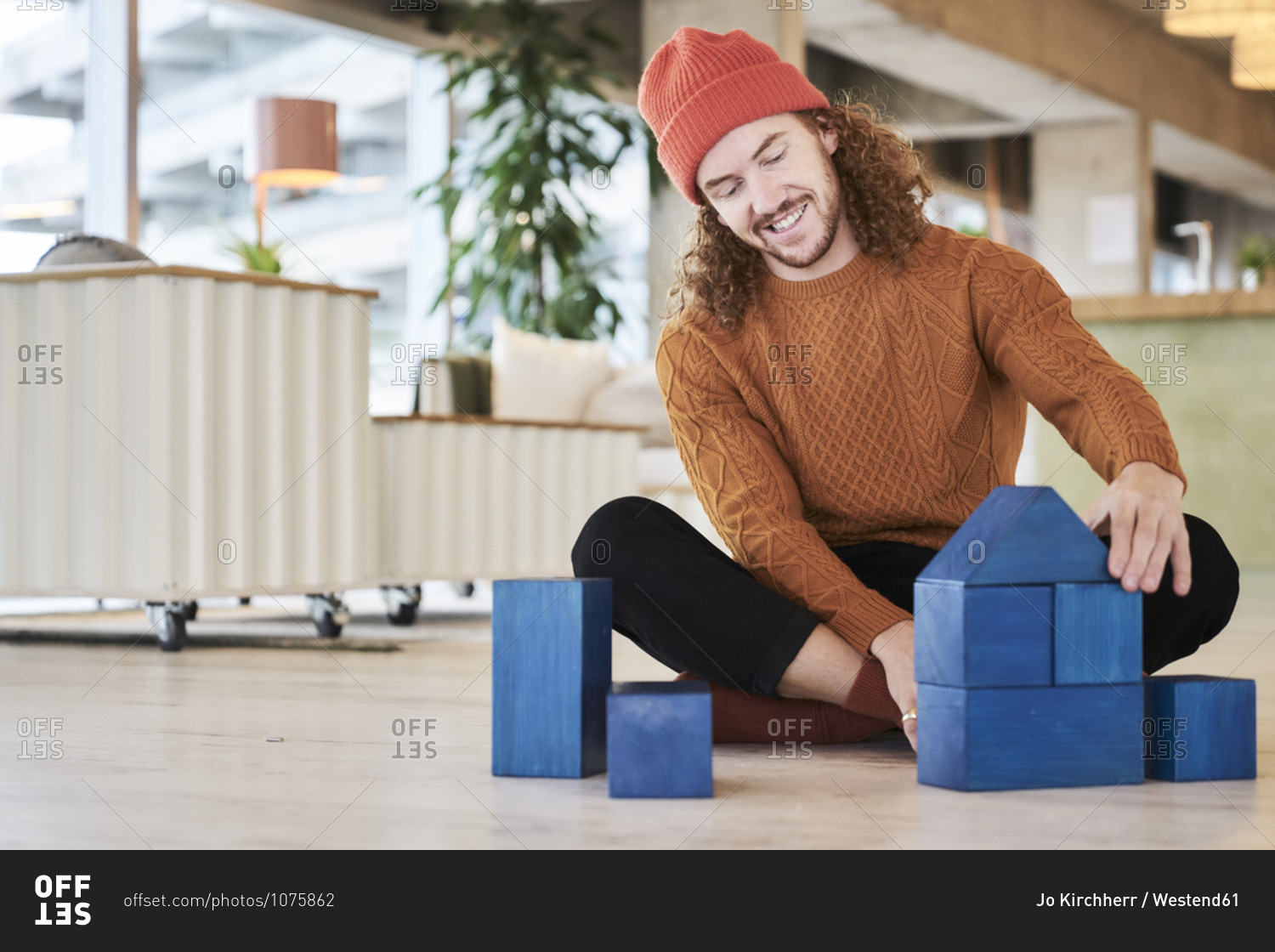 Hipster man playing with toy block while sitting on floor in living room at home