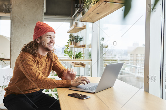 Smiling man wearing knit hat using laptop sitting at home
