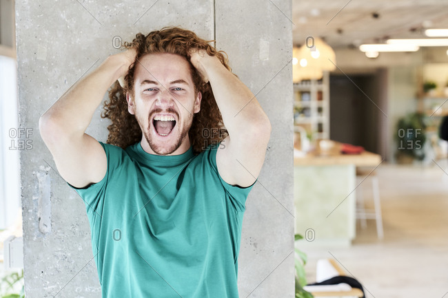 Angry man with hands in hair shouting while standing against column in living room at home