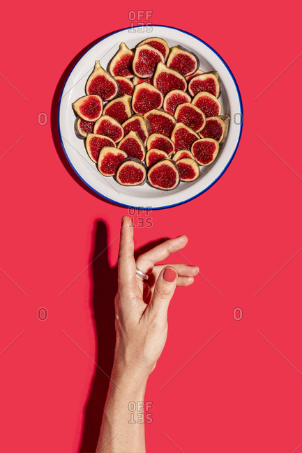 Directly above shot of woman hand by fig slices arranged in plate over red background