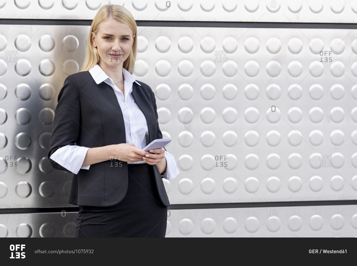 Blond businesswoman using mobile phone while standing against silver wall