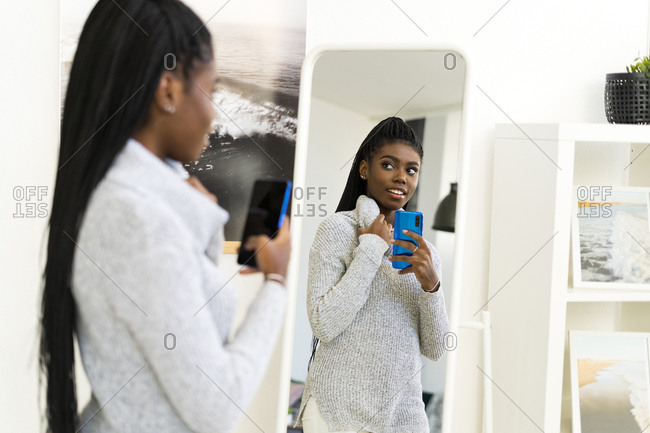 Young woman taking selfie through mirror reflection at home