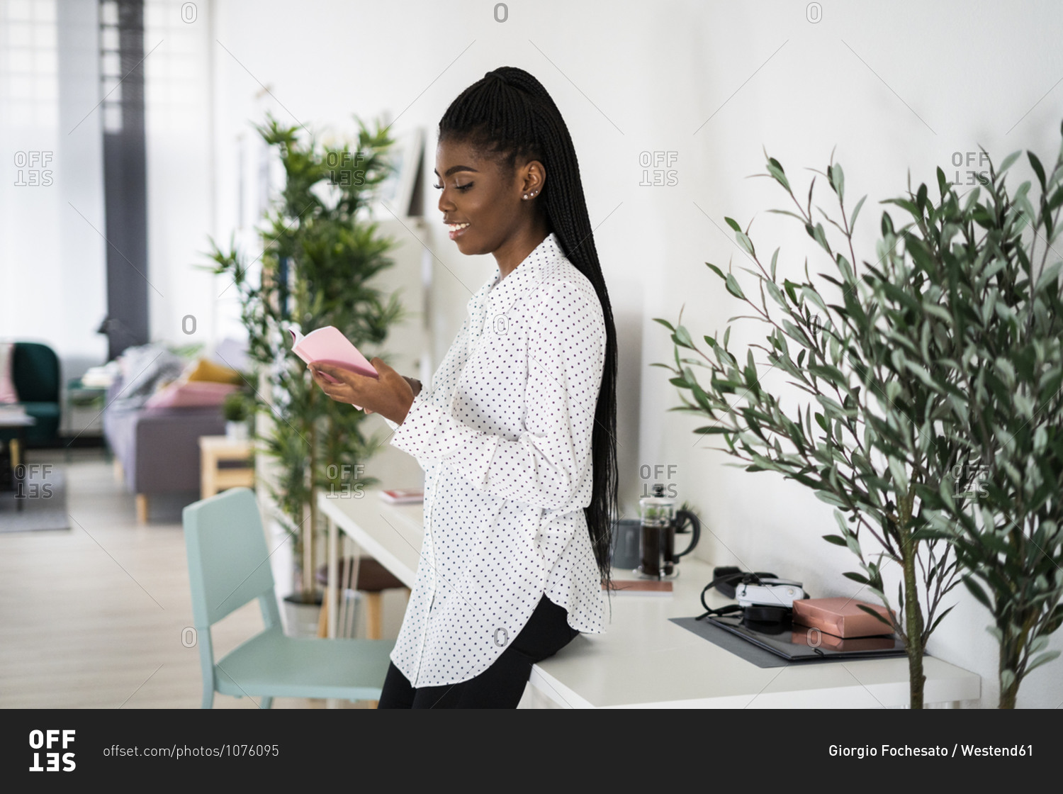 Smiling young woman reading book while standing at home