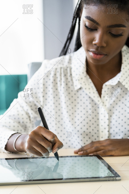 Woman concentrating while writing on digital tablet sitting in living room at home