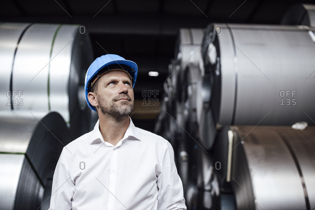 Thoughtful male owner wearing hardhat looking up while standing in factory