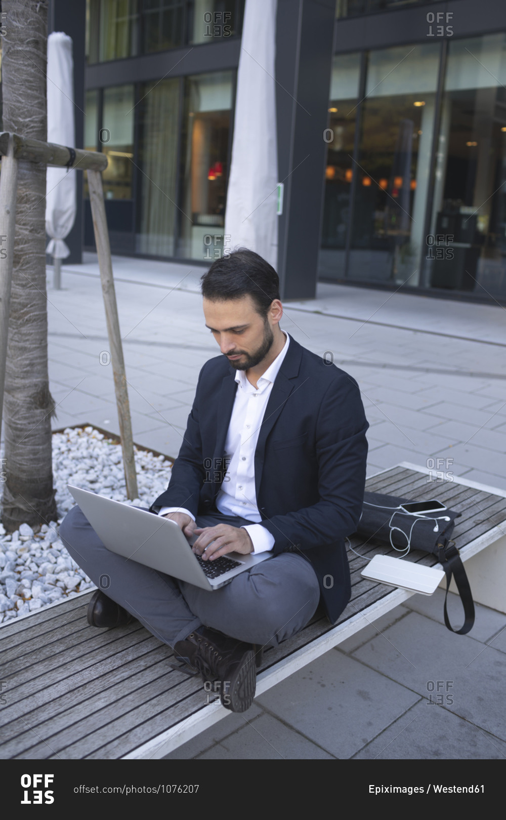 Confident businessman using laptop while sitting on bench in city