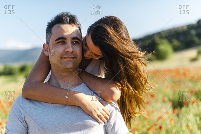 Girlfriend embracing boyfriend from behind at agricultural field during springtime